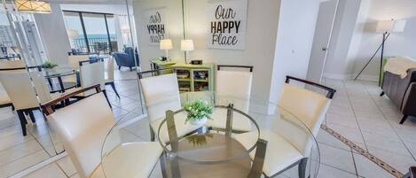 A modern dining area with a glass table and chairs, a small plant, and a wall with motivational text.