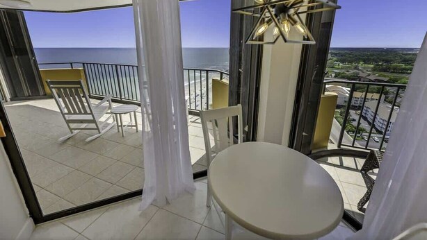 Un balcon avec une table et des chaises, une horloge et une vue sur l’océan.
