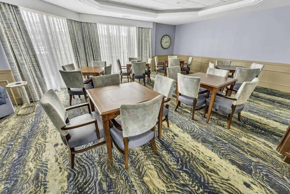 Uma sala de conferência com uma mesa grande e várias cadeiras, um relógio na parede e um tapete estampado.