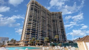 Un hôtel de grande hauteur doté de nombreux balcons, d’une piscine et de chaises longues.