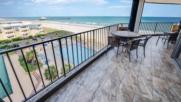 Un balcon avec vue sur la plage et l’océan, une piscine et un espace salon extérieur.
