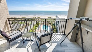 Un balcón con vista a la playa y la piscina, con una mesa y dos sillas.