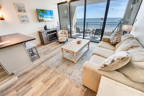 Una sala moderna con sofá, mesa de centro y televisor. Tiene un balcón con vista al mar.