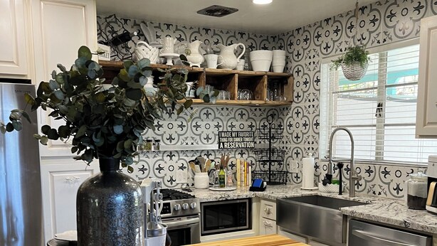 Een moderne keuken met witte kastjes, een houten tafel en een vaas met groene planten.