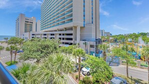 A high-rise hotel with multiple floors, a parking area, and a view of the beach.