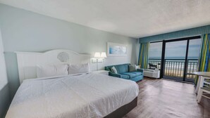 Une chambre d’hôtel avec un grand lit, un canapé bleu, un balcon donnant sur la mer et un tableau accroché au mur.
