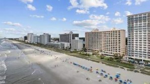 Un hôtel en bord de mer offrant une vue sur la plage, avec plusieurs étages et une rangée de parasols.