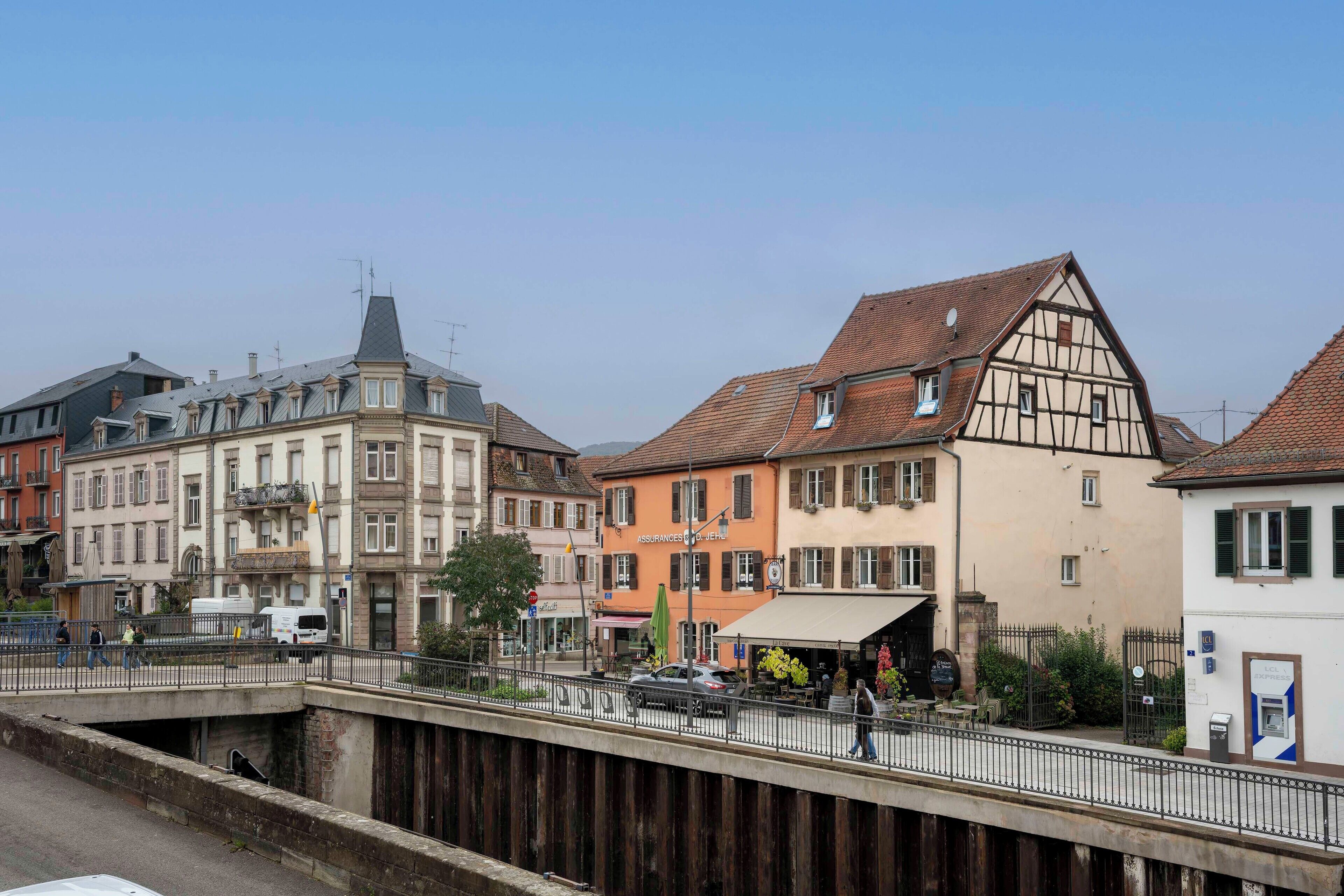 A street view with a variety of buildings, including a half-timbered house and a modern building with a sloped roof.