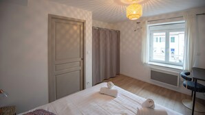 Une chambre d’hôtel avec un lit, un bureau, une fenêtre avec des rideaux, un radiateur et une porte.