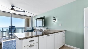 Een keuken met witte kastjes, een granieten aanrechtblad en uitzicht op de oceaan door een schuifdeur.