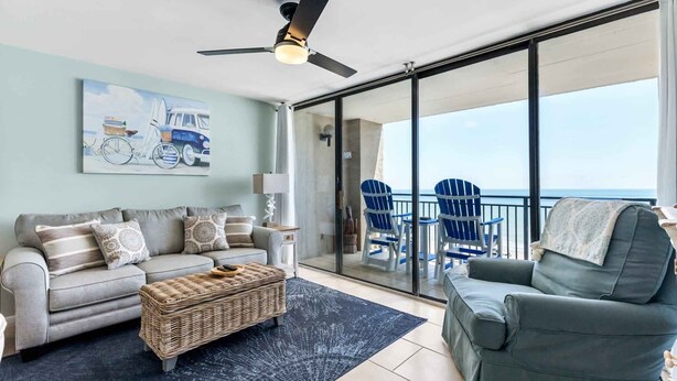 Een moderne woonkamer met een bank, een stoel, een rieten bijzettafeltje en een balkon met stoelen met uitzicht op de oceaan.