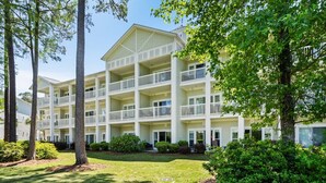 A multi-story hotel with balconies, a lawn, and surrounding trees. - World Tour Golf Resort Unit 103 - Golf view (Myrtle Beach)