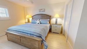 A bedroom with a wooden bed, two bedside tables with lamps, a small nightstand, and a window with blinds.