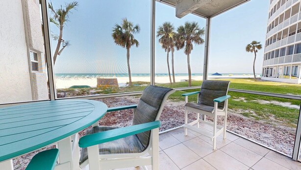A balcony with a view of the beach, equipped with a table and two chairs.