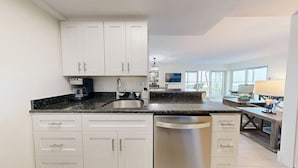 A modern kitchen with white cabinets, a stainless steel sink, and a coffee maker.