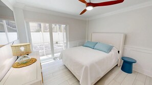 A bedroom with a bed, a ceiling fan, a lamp, and a view through a sliding door. - Crescent Arms 103S Siesta Key Florida (Sarasota)