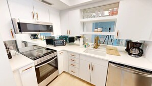 A modern kitchen with white cabinetry, a built-in oven, a microwave, a coffee maker, and a dishwasher. - Crescent Arms Vacation Rentals 203N Siesta Key Florida (Sarasota)