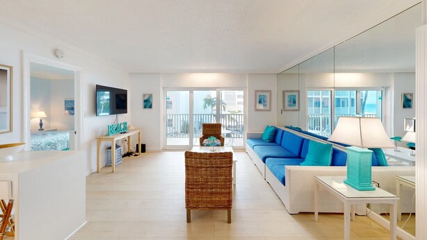A spacious living room with a large sofa, a television, and a balcony with a view. - Crescent Arms Vacation Rentals 203N Siesta Key Florida (Sarasota)