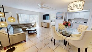 A modern living room with a sofa, a glass coffee table, and a dining area with chairs and a table.