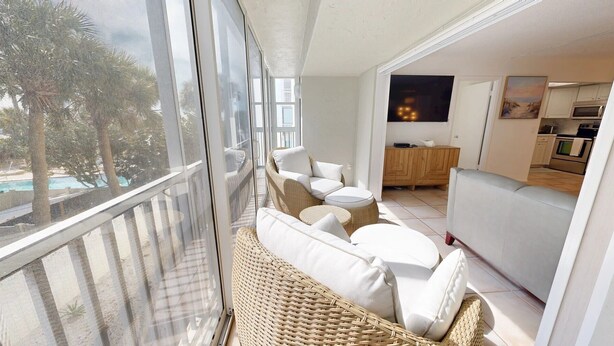 A balcony with wicker furniture and a view of a pool and palm trees.