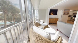 A balcony with wicker furniture and a view of a pool and palm trees.
