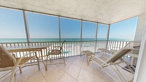 Un balcón techado con vistas a la playa, amueblado con sillas de mimbre y una mesa.