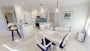 A modern kitchen with white cabinets, a central island, and a dining area with a white table and blue chairs. - Crescent Arms Vacation Rentals Villa 2 Siesta Key Florida (Sarasota)
