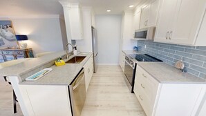 A modern kitchen with white cabinetry, a grey countertop, and a blue-tiled backsplash. - Crescent Arms Vacation Rentals Villa 2 Siesta Key Florida (Sarasota)