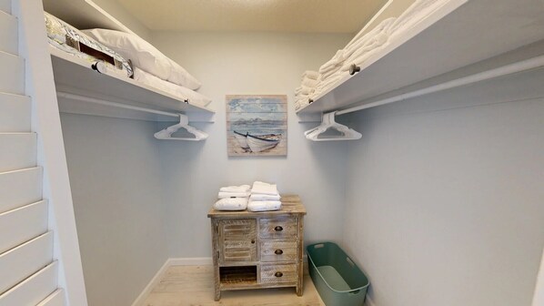 A narrow walk-in closet with white hanging space, a wooden dresser, and a beach-themed painting. - Crescent Arms Vacation Rentals Villa 2 Siesta Key Florida (Sarasota)