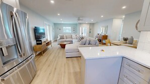 A modern kitchen with a built-in refrigerator, a dining area with a table and chairs, a sofa, and a ceiling fan. - Crescent Arms Vacation Rentals Villa 9 Siesta Key Florida (Sarasota)
