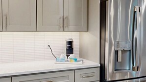 A kitchen with a stainless steel refrigerator, a coffee maker, and a set of cleaning supplies on the counter. - Crescent Arms Vacation Rentals Villa 9 Siesta Key Florida (Sarasota)