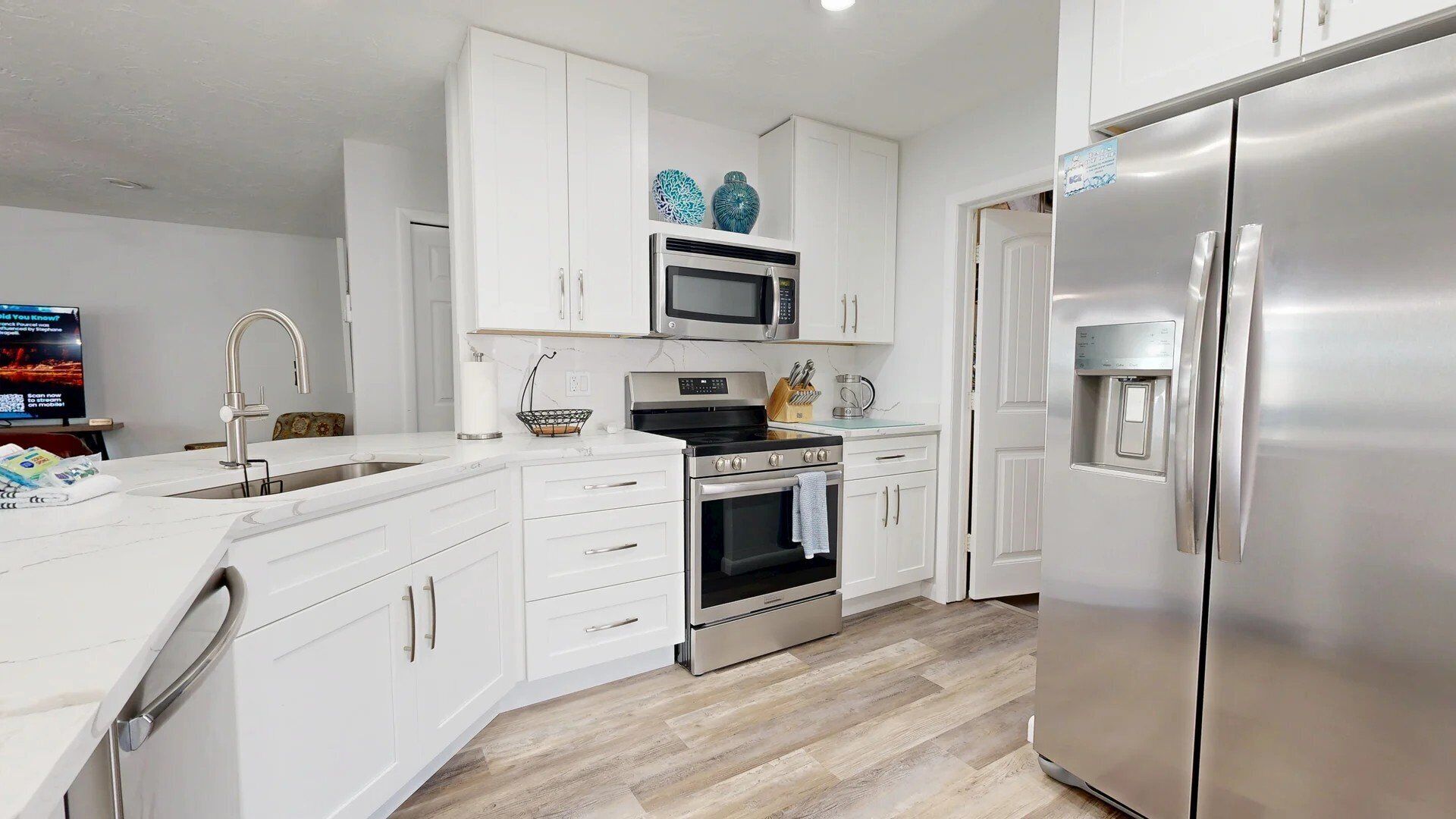 Una cocina moderna con armarios blancos, electrodomésticos de acero inoxidable y piso de madera.