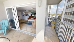 Ein Balkon mit Blick auf eine Wohngegend, eine Schiebetür, die zu einem Wohnzimmer führt, und ein blauer Sessel.