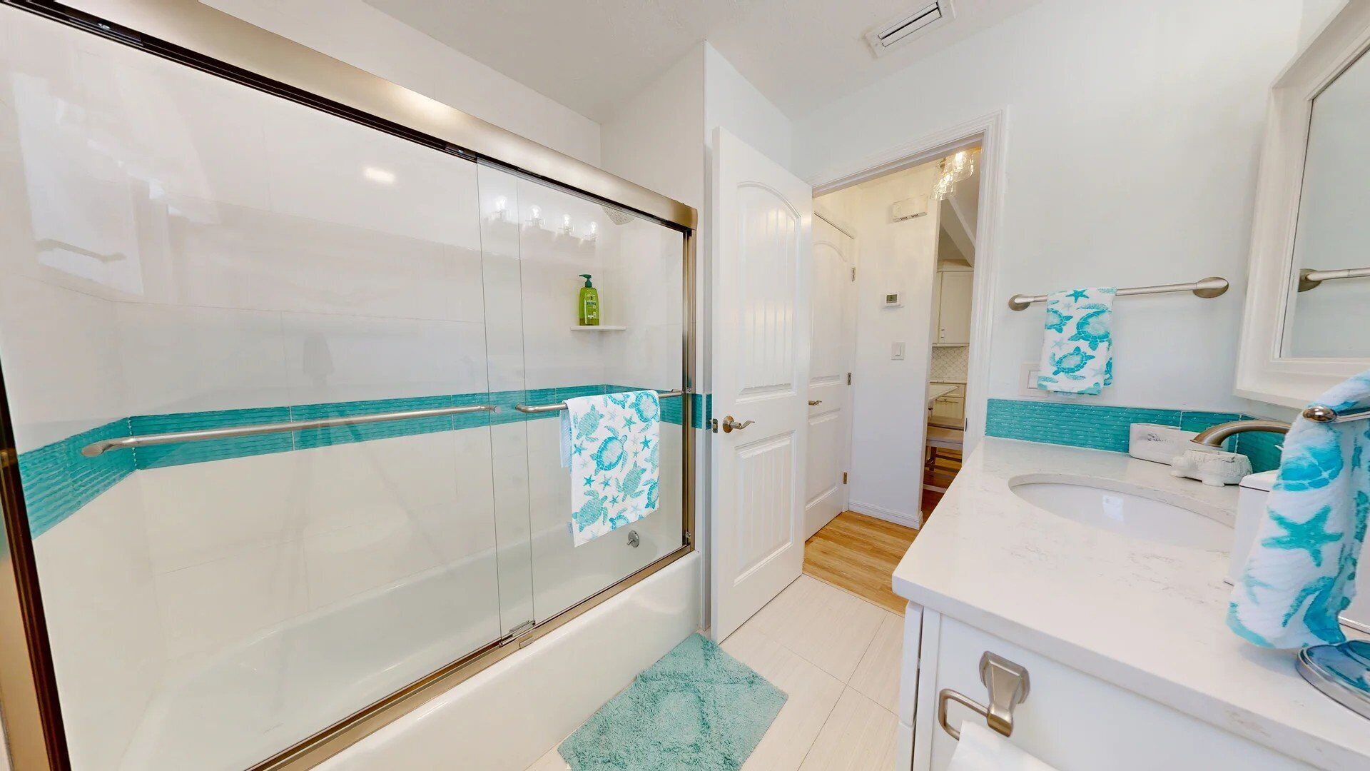 A modern bathroom with a glass shower enclosure, a white sink with a blue towel, and a wooden floor.