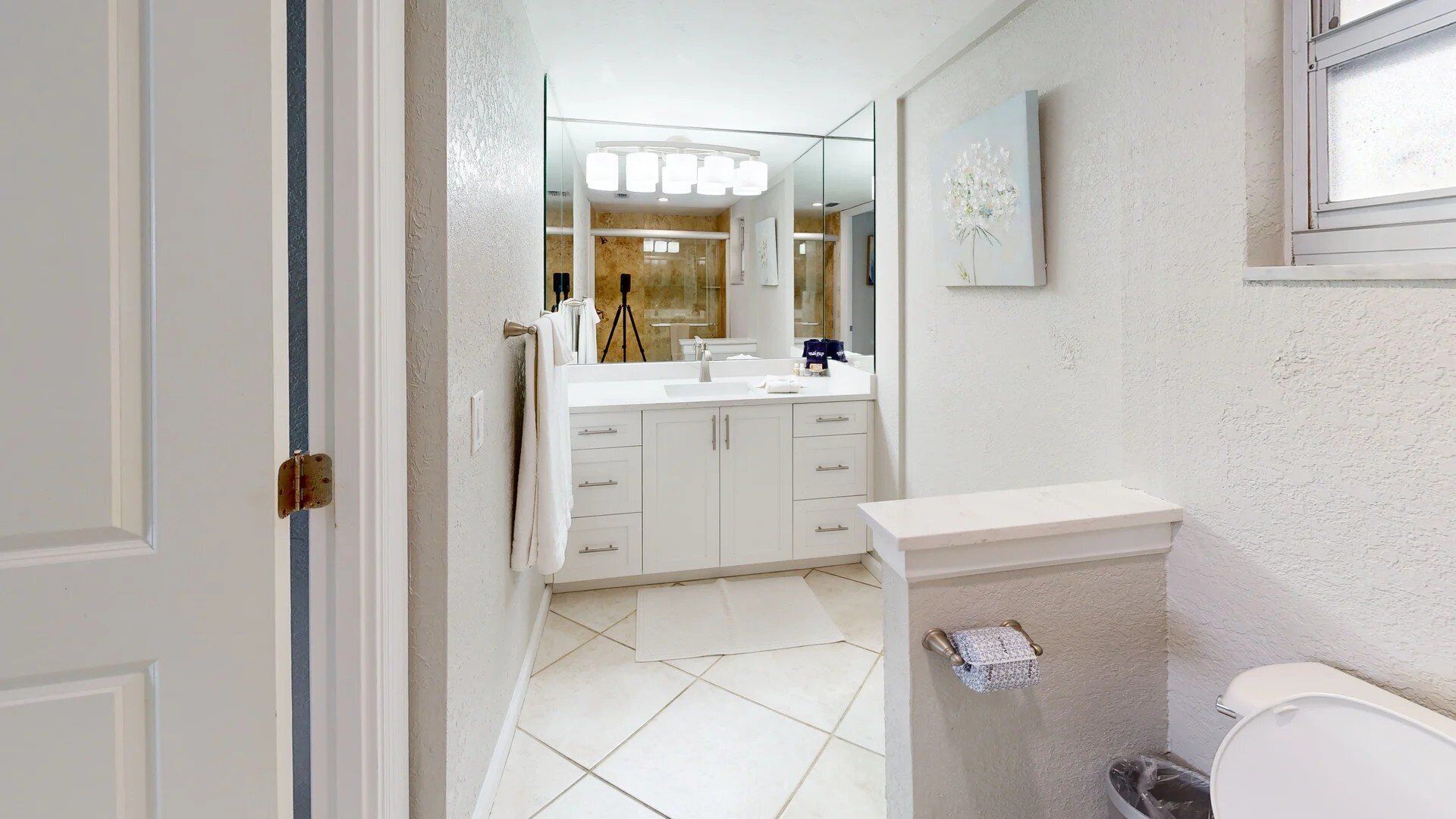 A modern bathroom with a large mirror, white cabinetry, and a toilet.