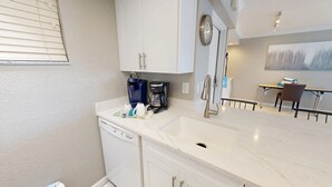 A modern kitchen with white cabinets, a marble countertop, a coffee maker, and a dishwasher. - Crescent Arms Vacation Rentals 702 N Siesta Key Florida SEPTEMBER 25% off (Siesta Key)