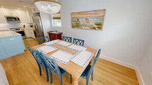 A dining area with a wooden table, blue chairs, and a painting of a beach scene.