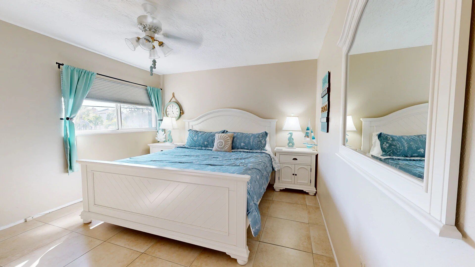 A bedroom with a bed, nightstands, a ceiling fan, a window with curtains, and a mirror.