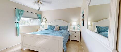 A bedroom with a bed, nightstands, a ceiling fan, a window with curtains, and a mirror.