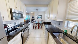 A modern kitchen with white cabinets, a black countertop, and a dining area with a round table and chairs.