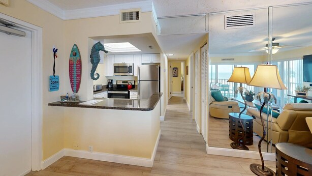 A modern kitchen with a central island, a dining area with a yellow sofa, and a view of the ocean through large windows. - Crescent Arms Vacation Rentals 204N Siesta Key Florida DISCOUNTS! (Siesta Key)