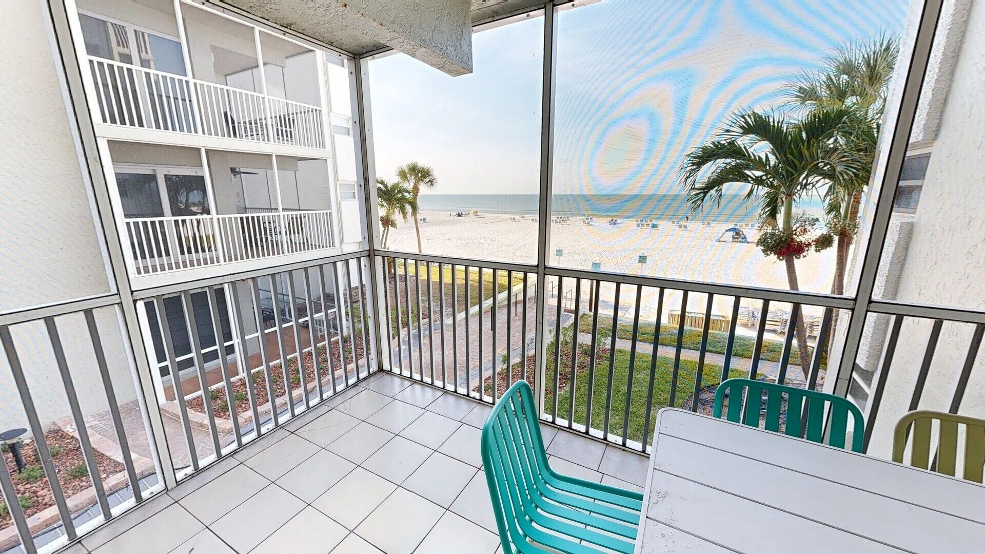 A balcony with a view of the beach, a table, and two chairs.