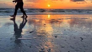 Une personne se promène sur une plage au coucher du soleil, et on peut voir le soleil près de l’horizon.