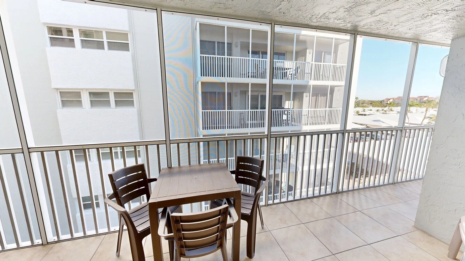 A balcony with a table and chairs, overlooking a building with multiple balconies.