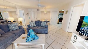 A living room with two grey sofas, a coffee table, and a TV on a stand. - Crescent Arms Vacation Rentals 405S Siesta Key Florida (Sarasota)