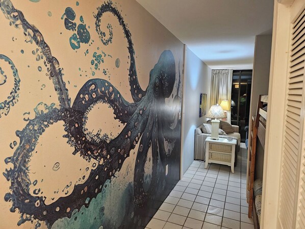 A hallway with a large octopus mural on the wall, a sofa, a lamp, and a window with curtains.