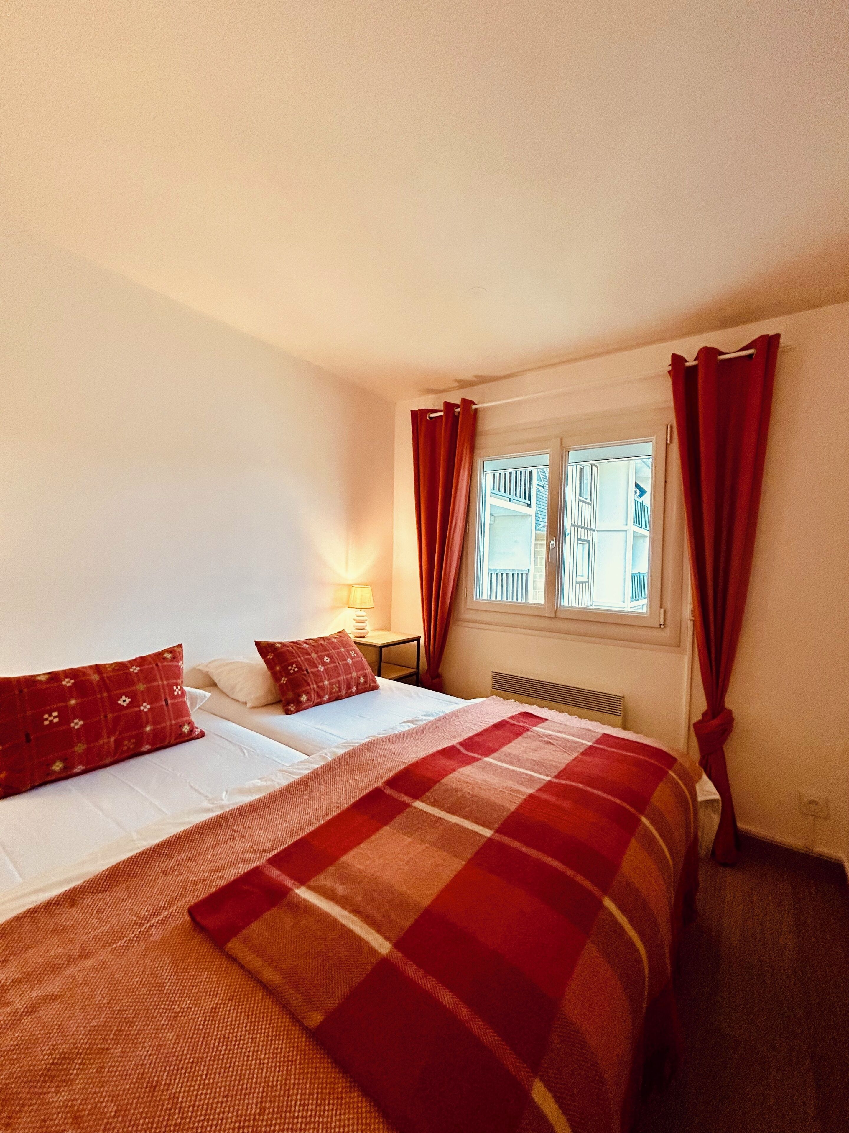 A bedroom with a bed, a nightstand, a window with curtains, and a radiator.