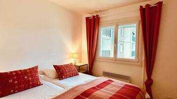 A bedroom with a bed, a nightstand, a window with curtains, and a radiator.