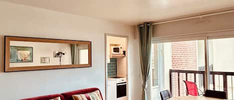 Een woonkamer met een rode bank, een eettafel met stoelen, een keukenhoek en een balkon met uitzicht.