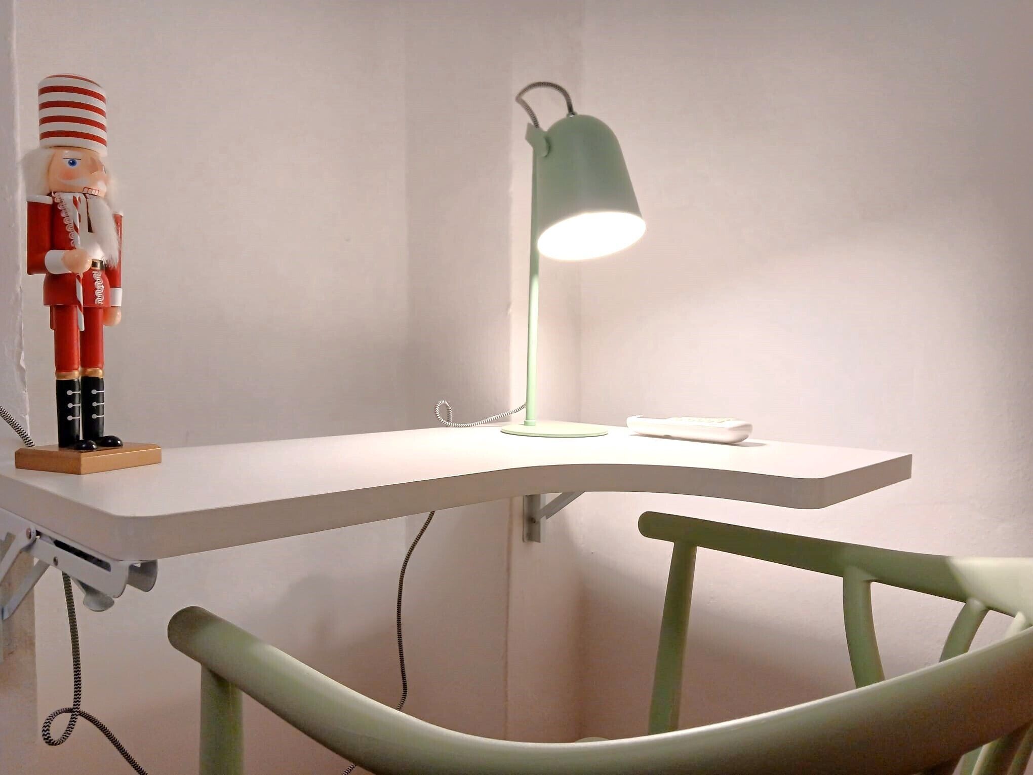 A white desk with a green desk lamp, a white chair, and a nutcracker figure.